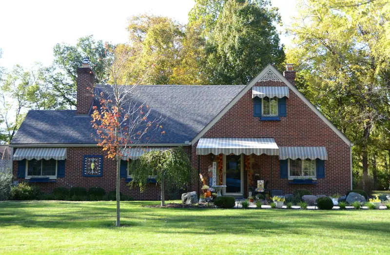 Older brick cottage with dormer windows surrounded by mature shade trees