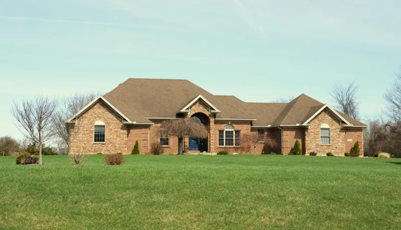 Brick and stone family home with trimmed shrubs and a manicured front lawn