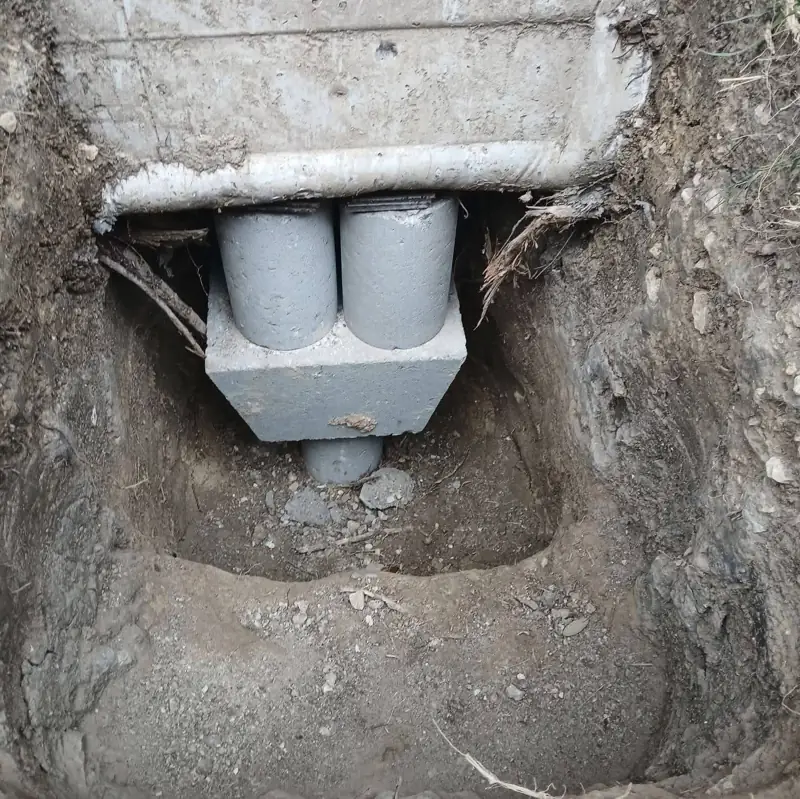 Excavated hole under a house showing a precast concrete pier pad and stacked cylinder blocks