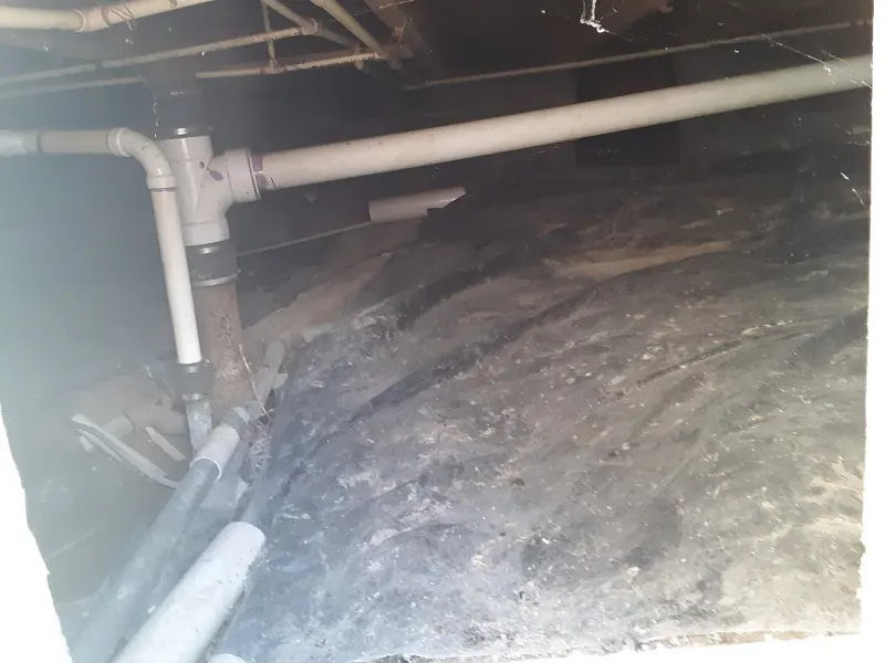 Low crawl space under a house showing the soil floor and support framing