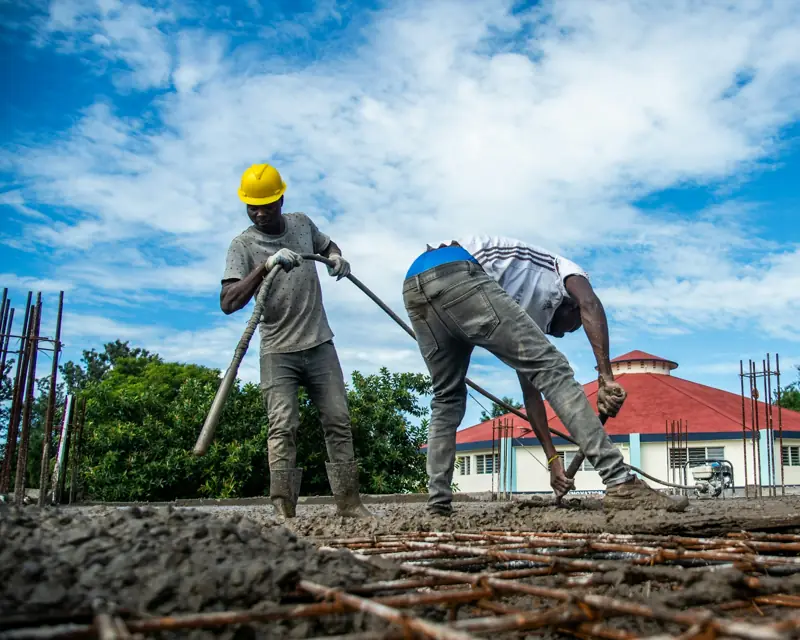 Construction crew in hard hats spreading fresh concrete over a rebar grid