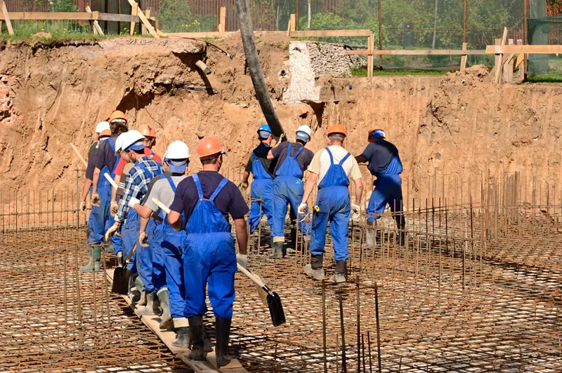 Construction crew pouring a concrete foundation into rebar-reinforced footings