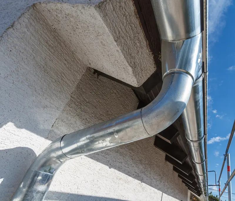 Metal downspout carrying roof water down a house wall to a ground drain