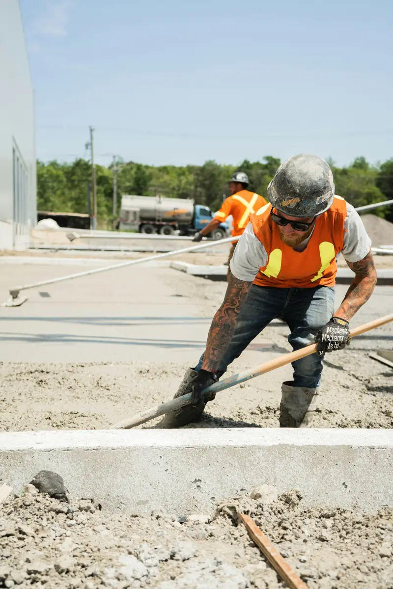 Worker in a hi-vis vest and hard hat placing concrete for a new slab